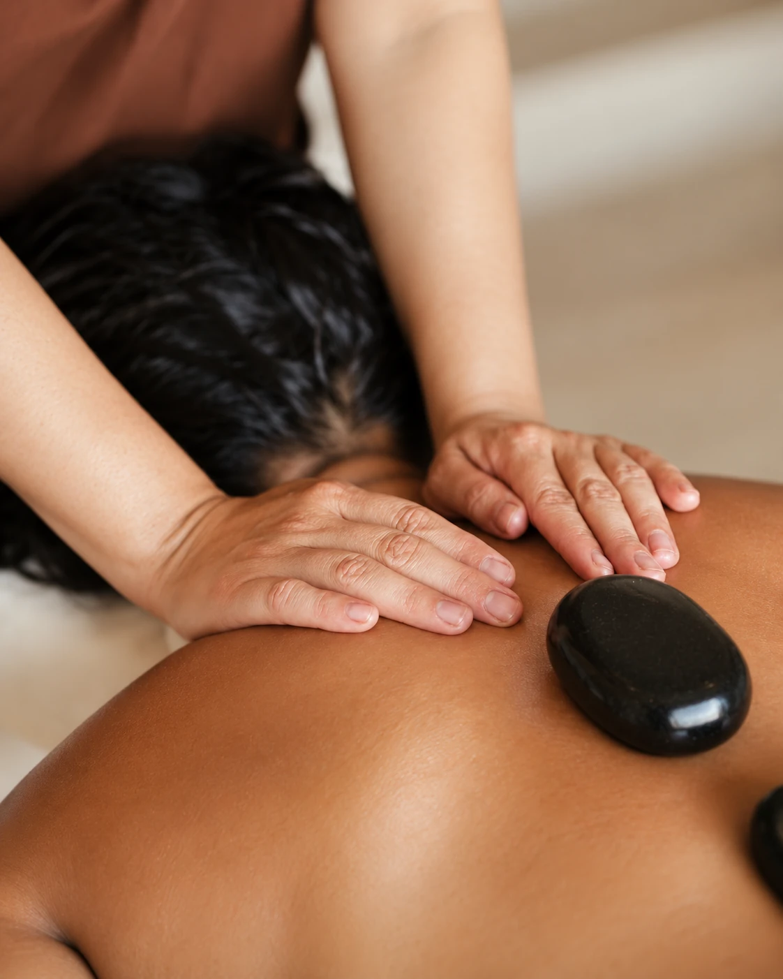 Handen van een specialiste van Studio Rosa tijdens een massage met warme stenen