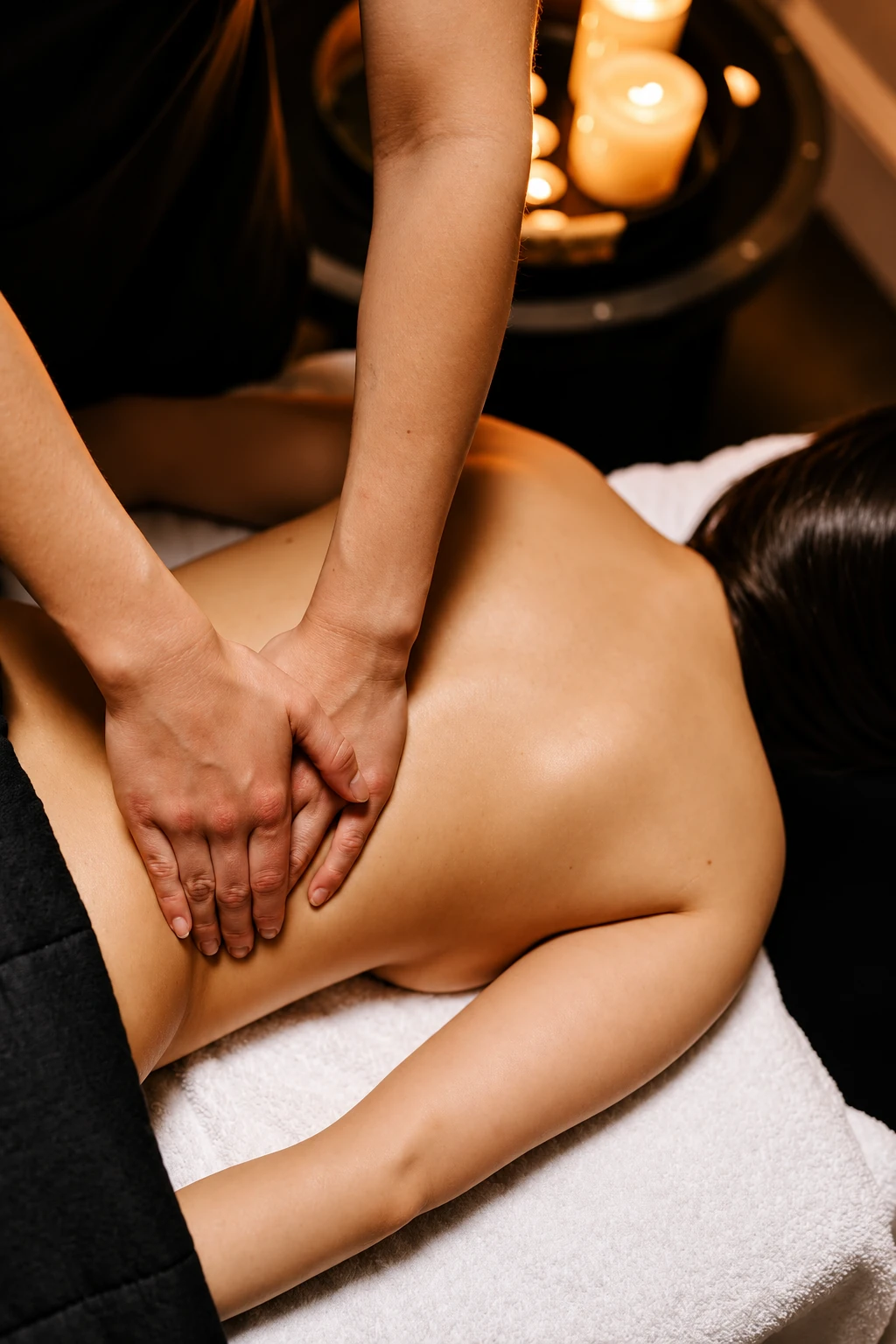 Handen van een specialiste masseren de rug van een gast bij kaarslicht